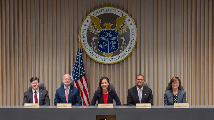 Five people sitting at a table with the logo of the Federal Communications Commission behind them.