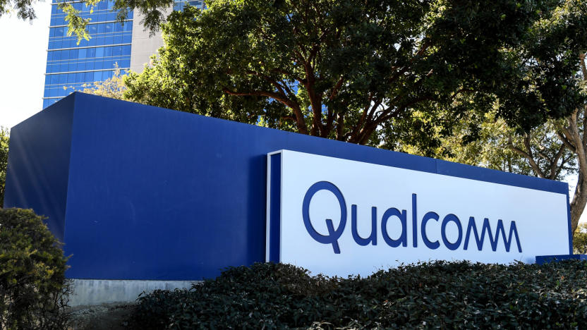 A sign that says Qualcomm with trees and a building in the background.