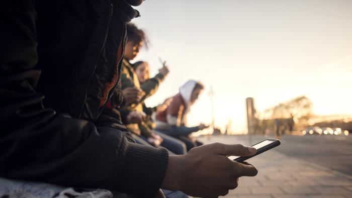 Midsection of teenager using phone while sitting with friends by cobbled street