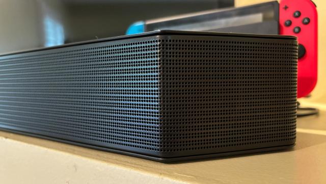 Samsung Q990D soundbar's front right corner with a TV and a Nintendo Switch console in the background.