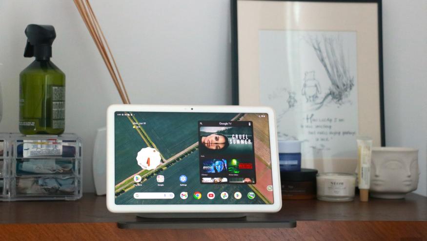 The Pixel Tablet on its dock on a walnut chest of drawers showing the Android home screen.